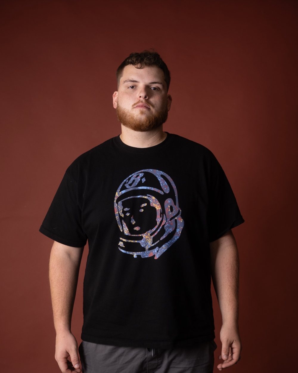 Tanner Castille standing against a rust-red studio backdrop